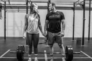 Mike and Vickie standing in front of a barbell while holding hands and gazing into each other's eyes.